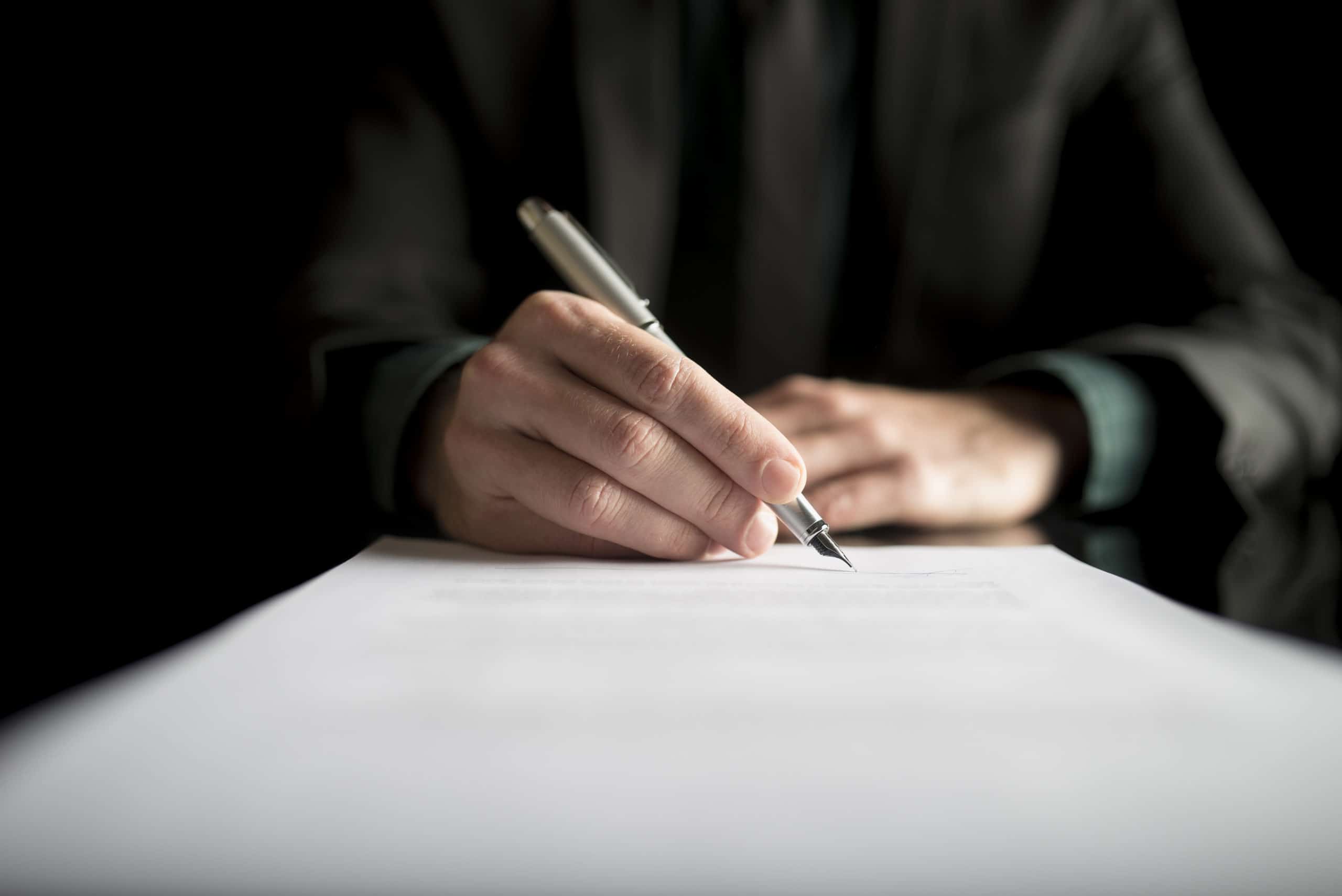 Closeup of lawyer or executive signing a contract, placed on black desk.