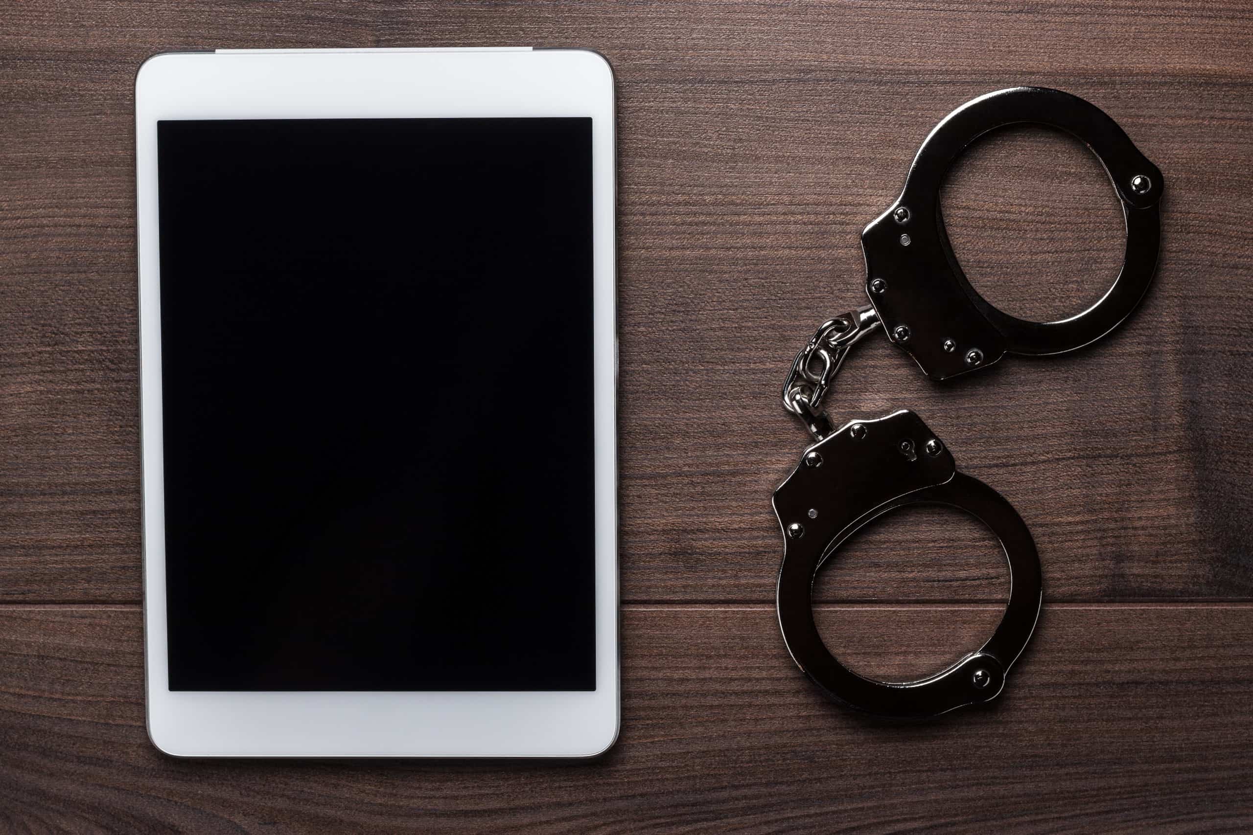 handcuffs and tablet computer on brown wooden background