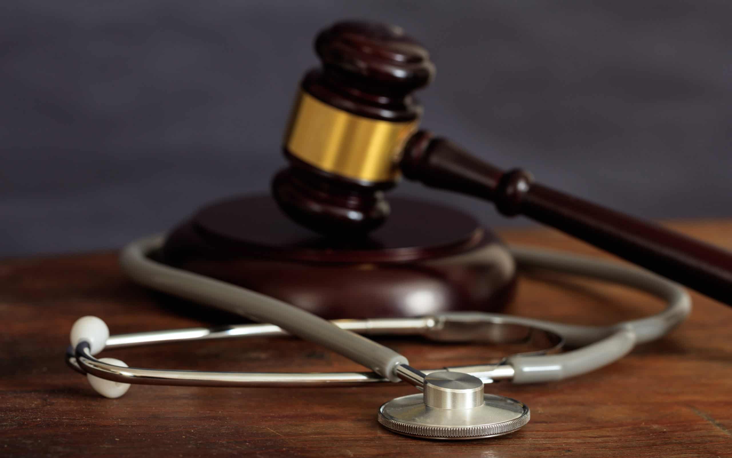 Law gavel and a stethoscope on a wooden desk, dark background